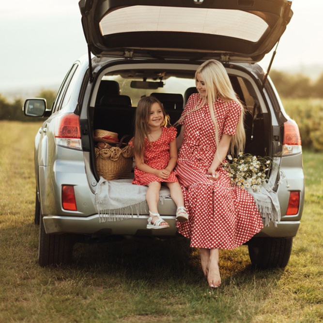 A woman and a young girl in red polka dot dresses sitting on the edge of an open car - arlingtonagency.com