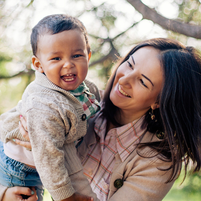 A woman holding a young child outdoors with trees in the background - arlingtonagency.com